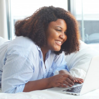pretty-plump-african-american-woman-greets-her-friend-online-while-lying-in-bed-with-a-laptop_186451-470 1