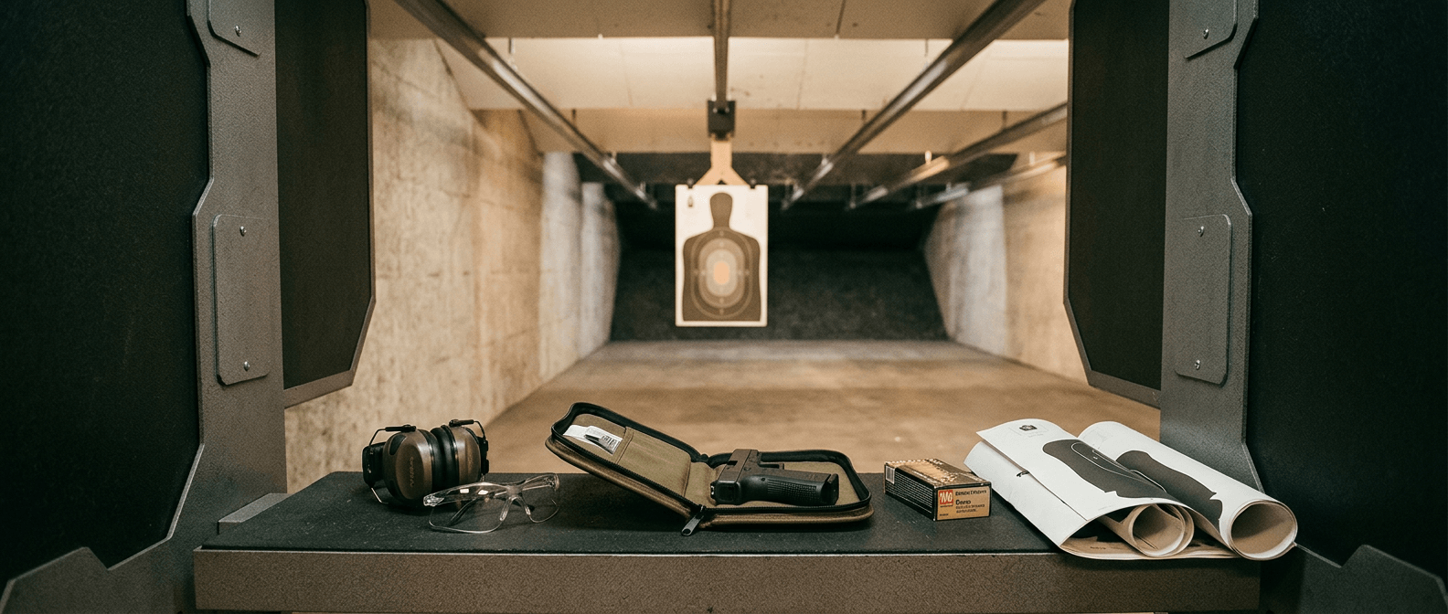 Indoor shooting range lane at Kjergaard Sports — ear protection, eye protection, handgun in case, ammunition, and silhouette target downrange