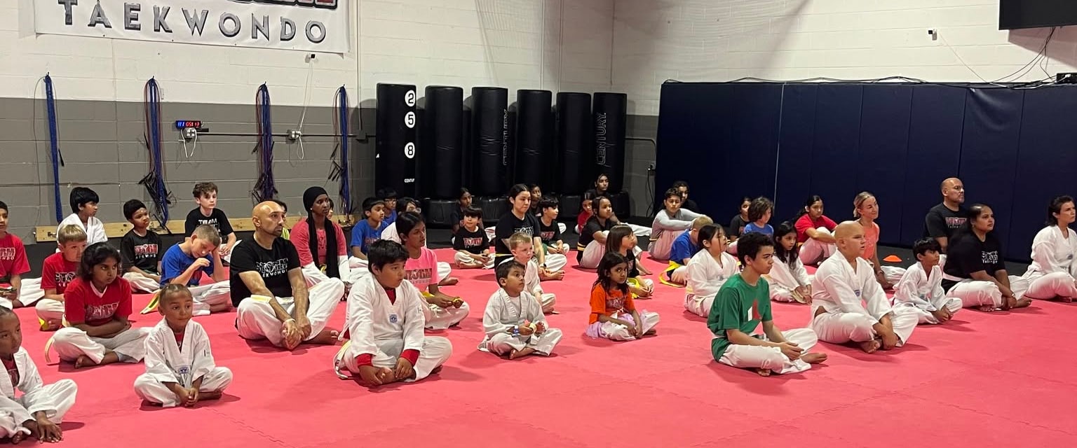 A mixed-age Storm class seated on the training mats for instruction